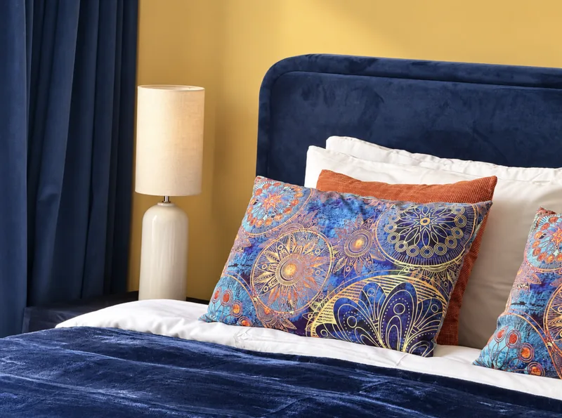 Navy velvet headboard with blue-and-gold mandala cushions against a yellow wall