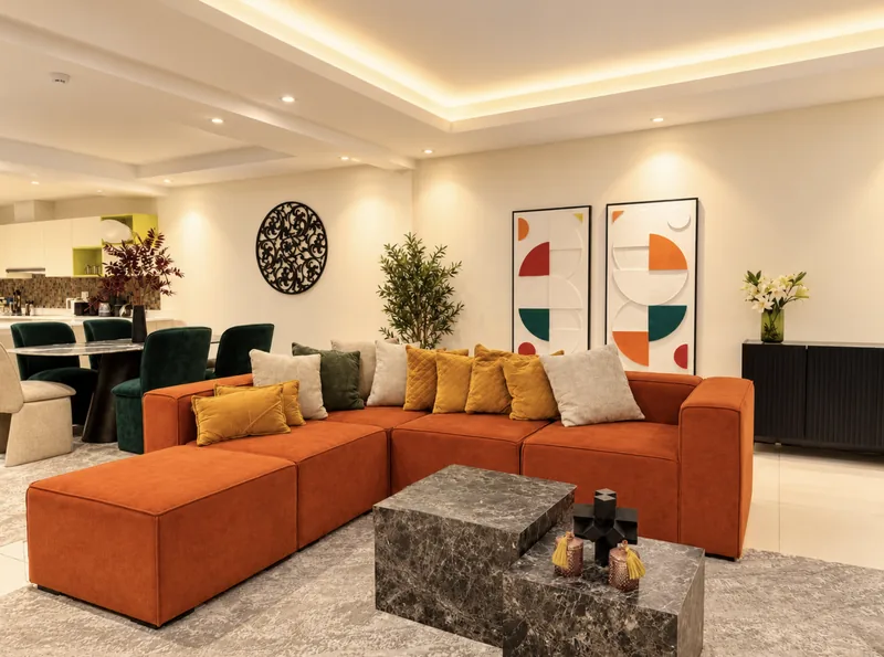 Dunia open-plan lounge with orange sofa and mustard cushions, geometric artworks and the dining table and kitchen behind