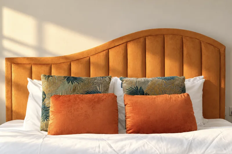 Orange velvet wave headboard with palm-print and orange cushions
