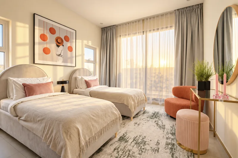Twin bedroom with pink cushions, pink velvet chair and sheer curtains