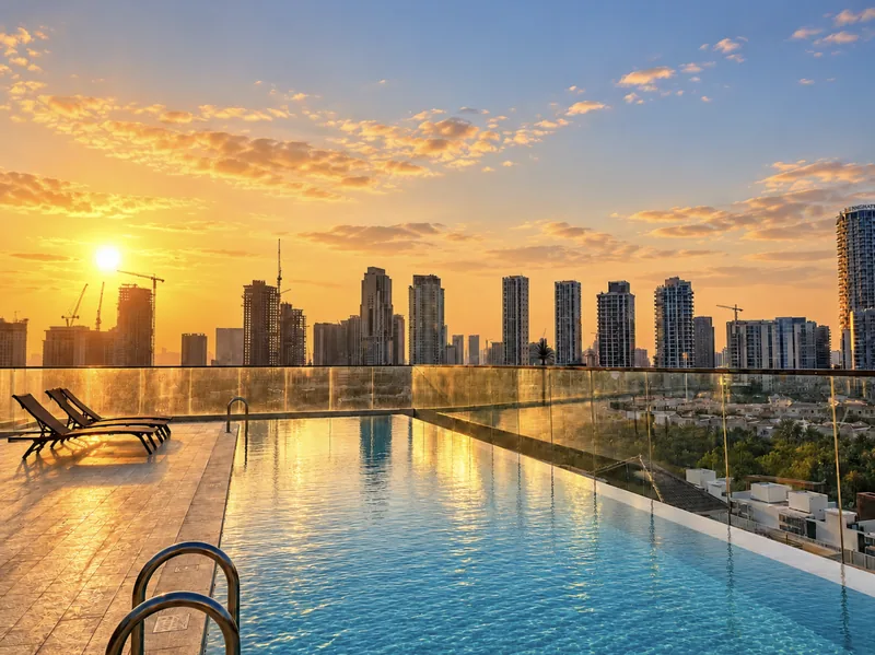 Rooftop infinity pool with sun loungers at sunset, overlooking the JVC skyline
