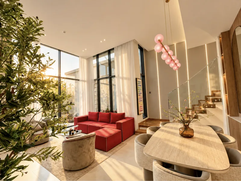 Pearl living and dining area with red sofa, oval dining table, pink globe chandelier and lit staircase