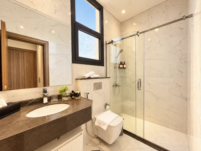 Yasmin bathroom with glass shower, marble walls and dark vanity