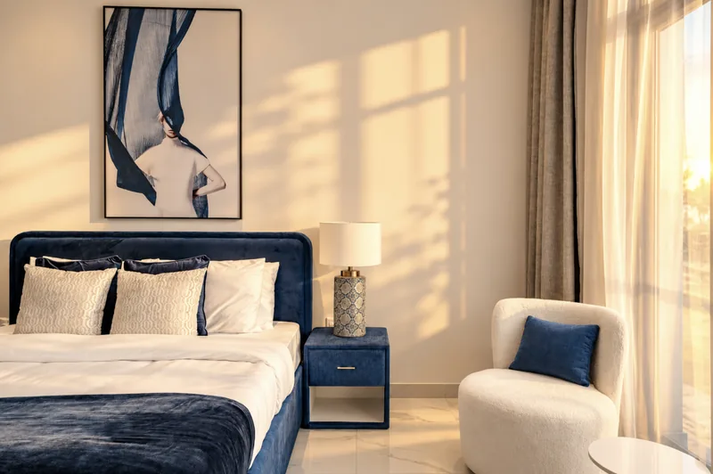 Zephyr bedroom with navy velvet bed, fashion print, bedside lamp and white armchair